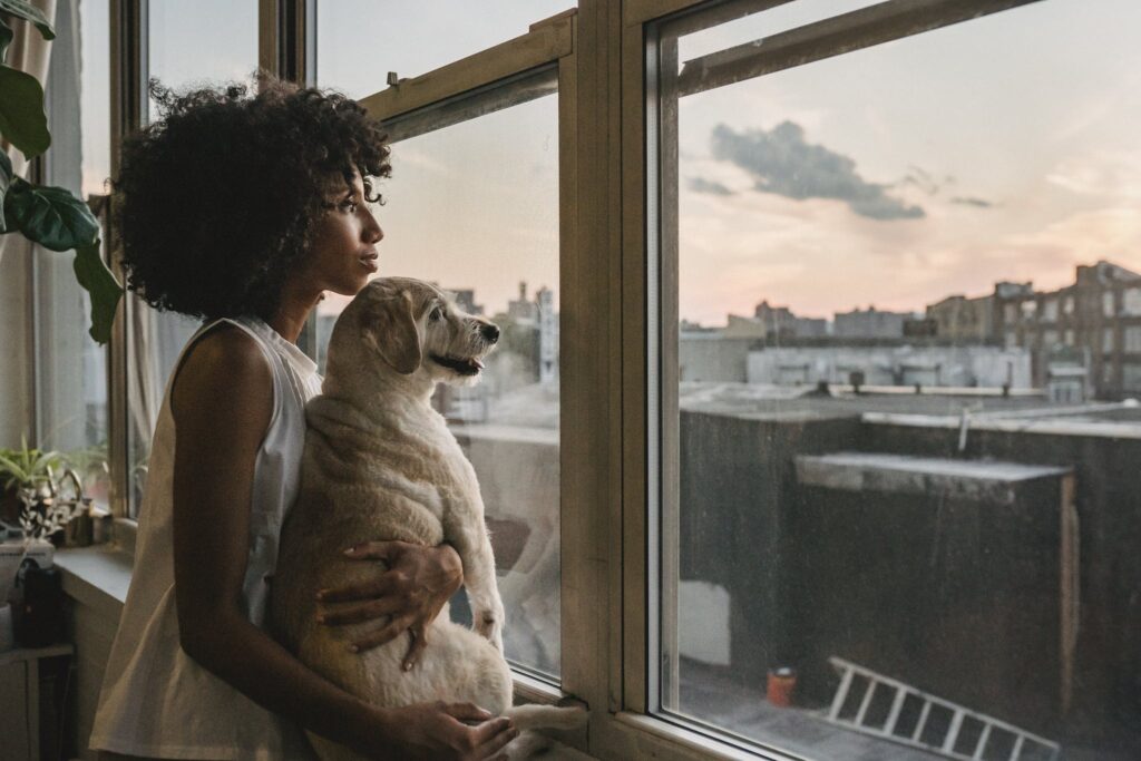 Woman cuddling dog while standing near window